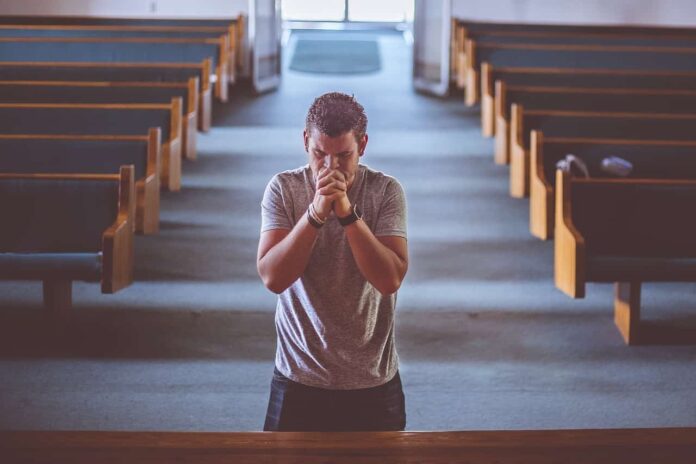 mężczyzna modli się klęcząc w kościele